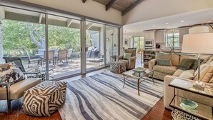 Amplia sala de estar con un gran ventanal que da a un patio exterior, un rincón de descanso acogedor con sofá y sillones, y una cocina al fondo.