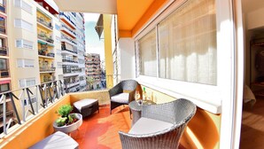 Un balcón con mobiliario de mimbre, una planta en maceta y vistas de la ciudad.