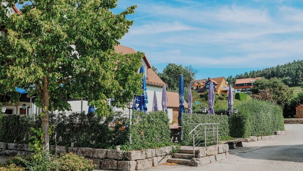 Un quartier résidentiel avec des maisons, un arbre et des espaces de détente en plein air, équipés de parasols.