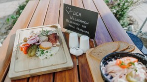 Une table de pique-nique en bois, sur laquelle on a disposé une planche de charcuterie, un saladier rempli de salade et un panneau accueillant les invités.