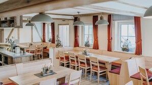 Un vaste espace dédié à la salle à manger, avec de nombreuses tables et chaises, des poutres en bois au plafond et de grandes fenêtres dotées de rideaux.