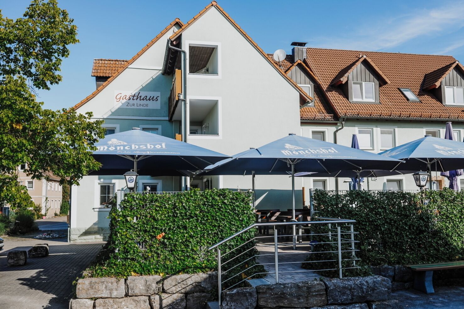Un edificio con un letrero que dice 'Gasthaus Zur Linde' y sombrillas exteriores con la leyenda 'Mönchsöli'.