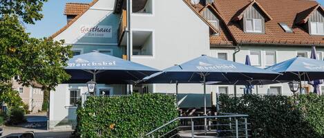 Un edificio con un letrero que dice 'Gasthaus Zur Linde' y sombrillas exteriores con la leyenda 'Mönchsöli'.