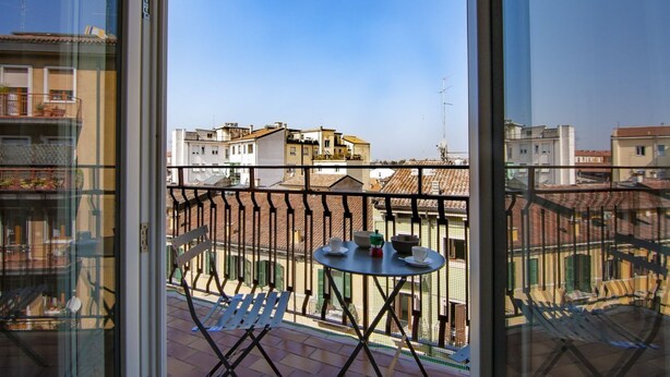 Un balcón con mesa y sillas, con vista a un paisaje urbano lleno de edificios.
