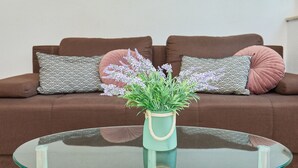 Un divano marrone con cuscini decorati, un tavolino in vetro con una pianta e un vaso azzurro chiaro.