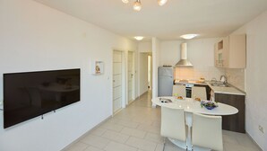 Una cucina moderna con una TV a schermo piatto, un'area pranzo con un tavolo e sedie bianche, e un corridoio che porta a un'altra stanza.