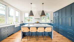 Een moderne keuken met een groot eiland, blauwe kastjes en hangende lampen.