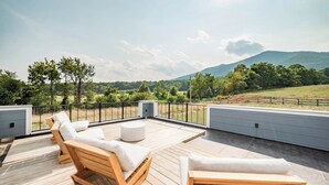 Een houten terras met lounge stoelen en een kleine tafel, met uitzicht op een schilderachtige omgeving met bomen en heuvels.