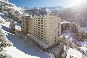 Un hôtel à plusieurs étages, doté d’une façade symétrique, entouré d’arbres et de montagnes couverts de neige.