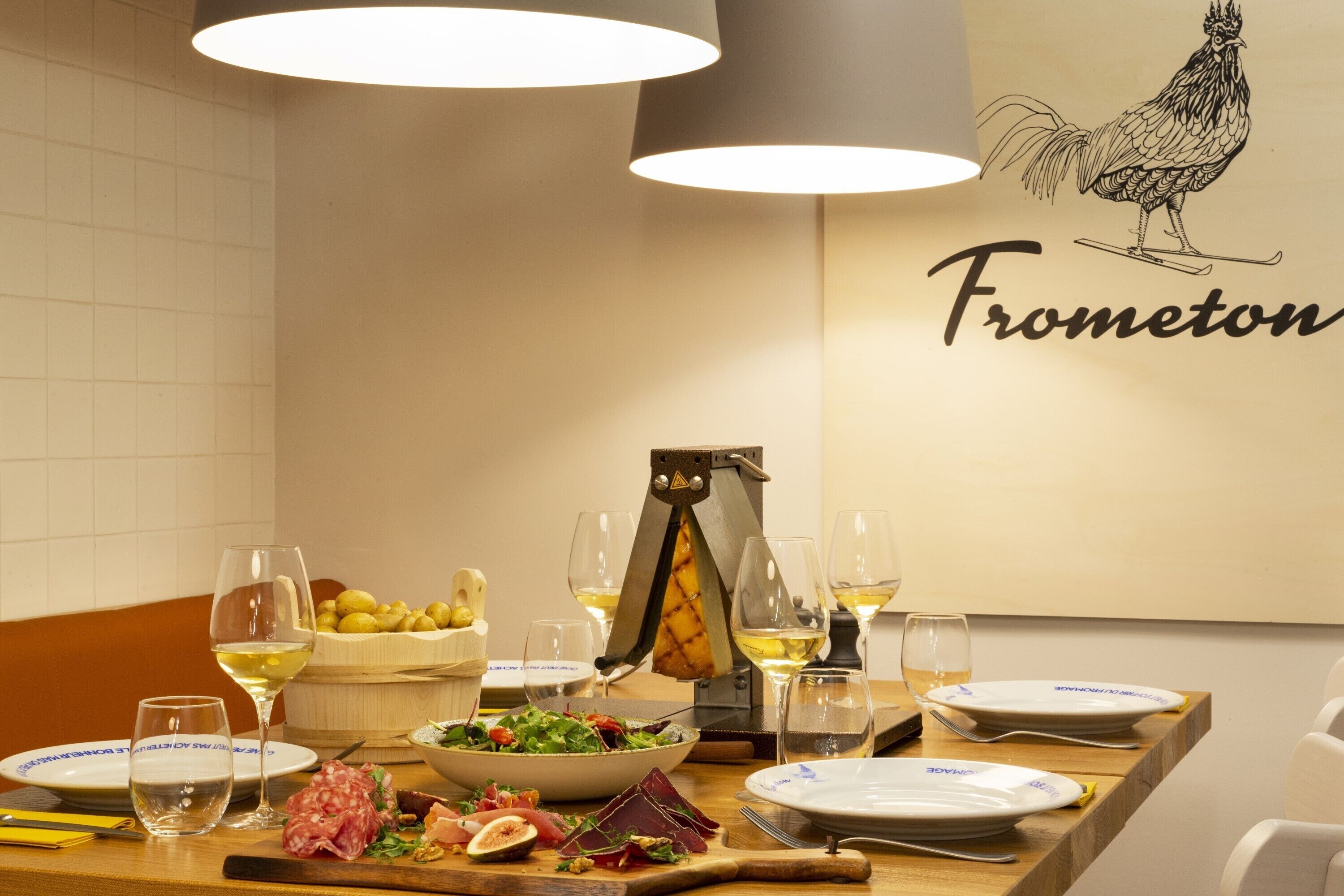 A dining table set with plates, glasses, a cheese slicer, a bowl of salad, and various meats.