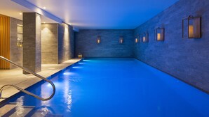 Une piscine intérieure moderne, avec une eau d’un bleu limpide, des murs en pierre et un éclairage encastré.