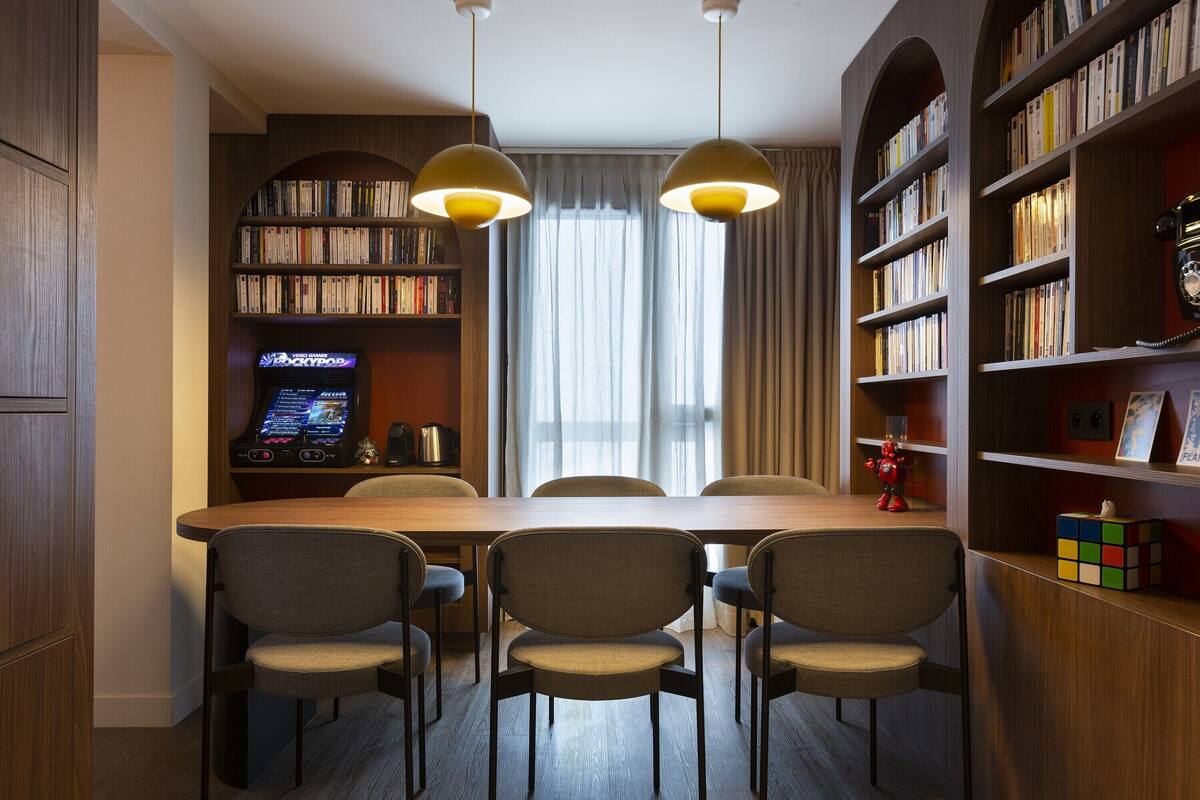 Une bibliothèque moderne avec une table et des chaises en bois, des étagères et un juke-box.