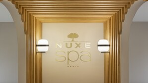 Une enseigne pour le spa NUXE à Paris, avec un logo représentant un arbre et deux lampes fixées au mur.