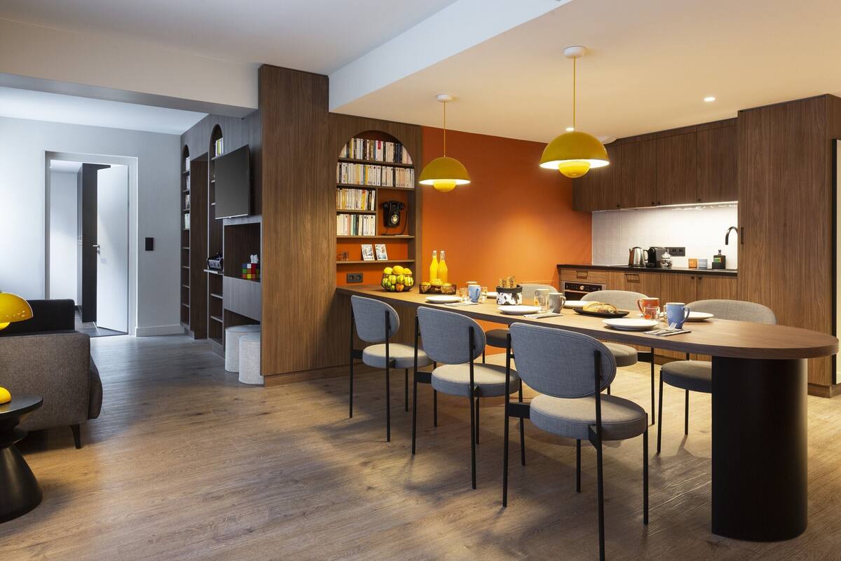 Une cuisine moderne avec des meubles en bois, une table à manger avec des chaises et des luminaires suspendus.