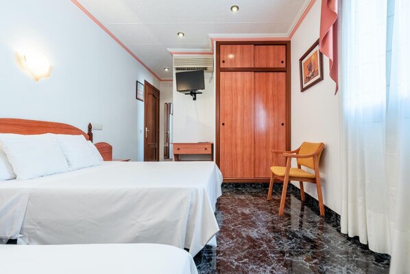Habitació d'hotel amb llit, escriptori, cadira, armari i televisió.