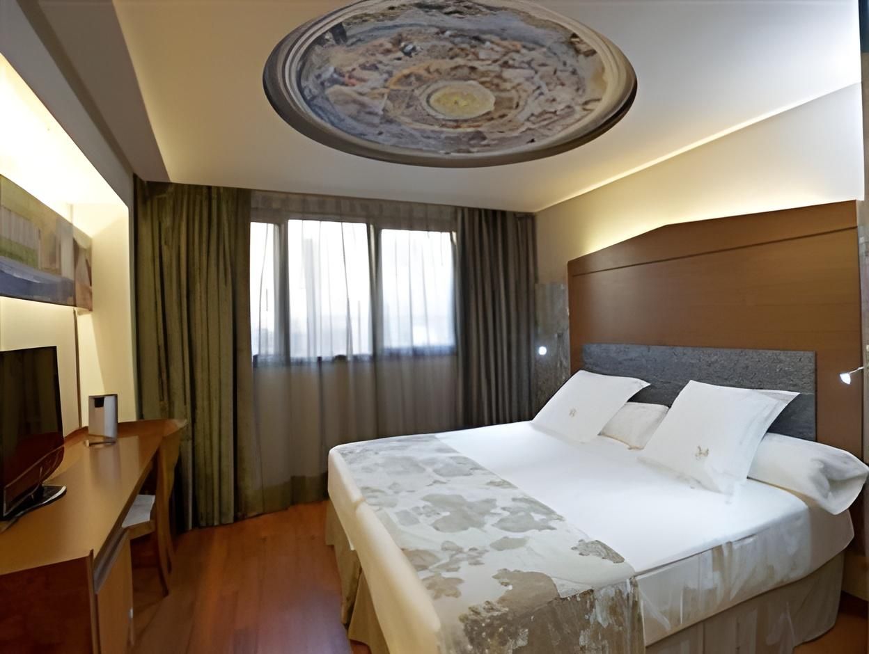 Habitación de hotel con cama, escritorio, televisor y techo con diseño circular.