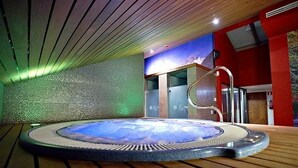 Un jacuzzi en una habitación con suelo de madera, una pared roja y un separador de vidrio.