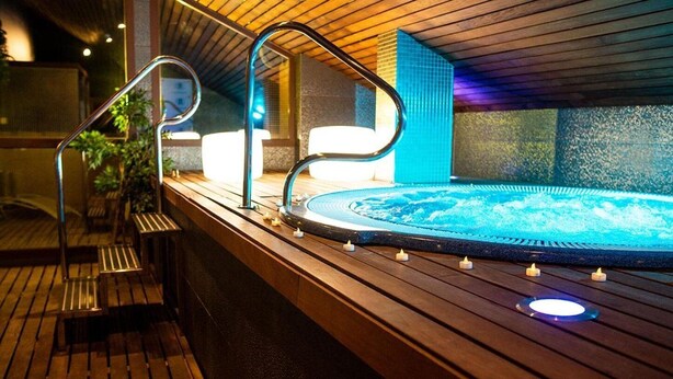Una terraza de madera con un jacuzzi, barandilla metálica y velas.