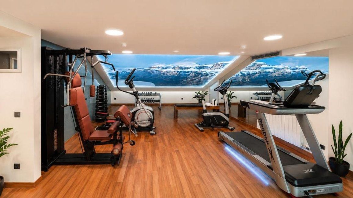 A gym with various exercise equipment, a treadmill, and a view of a snowy landscape through a large window.