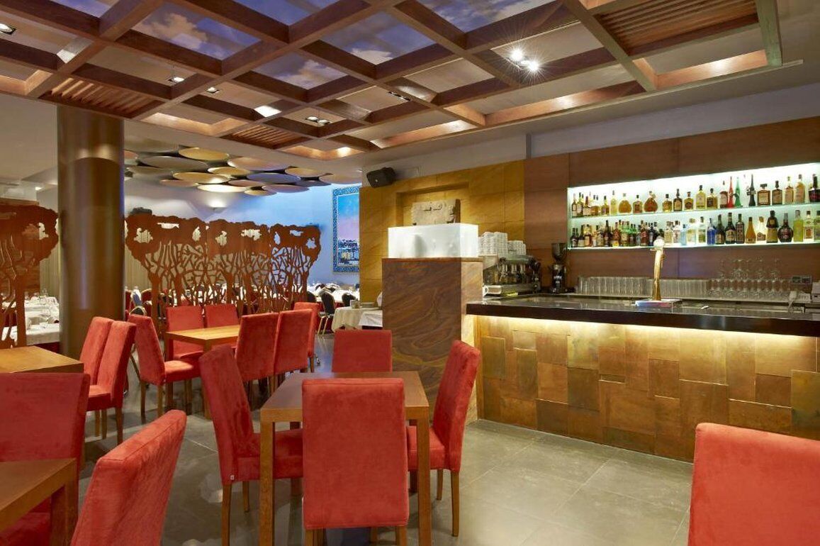 Un restaurant avec des chaises rouges, un coin bar avec des bouteilles et un plafond décoratif.