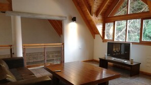 Een woonkamer met een houten tafel, een bank, een televisie op een meubel en een stenen muur.
