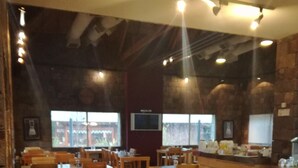 Een restaurant met houten tafels en stoelen, een bar en grote ramen.