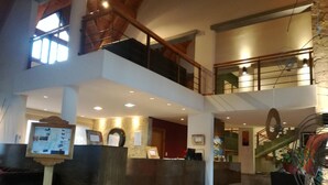 Een ruime lobby met een receptiebalie, een trap en een hoog plafond met zichtbare balken.