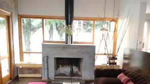 Een woonkamer met een open haard, een bruine bank, een roze poef en een salontafel.