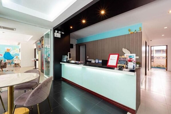 Zona de recepción de un hotel con diseño moderno, que incluye un mostrador de recepción, un área de descanso con una mesa redonda y sillas, y vistas al exterior.