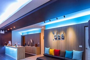 Un moderno vestíbulo de hotel con una recepción, una zona de estar con cojines coloridos y un letrero en la pared.