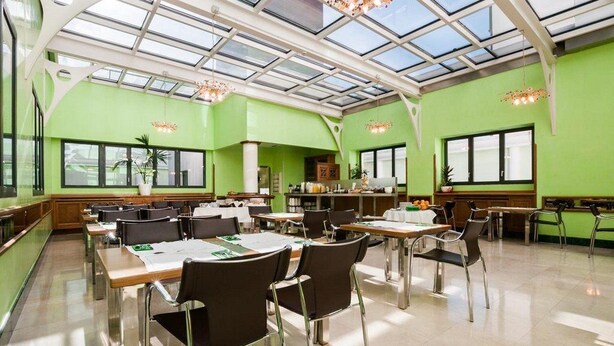 A spacious dining area with high ceilings and a skylight, featuring green walls and modern furniture. - Hotel Julia (Madrid)