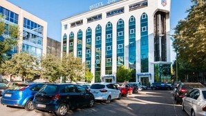 A modern hotel building with a prominent sign, multiple windows, and a parking lot with various cars. - Hotel Julia (Madrid)