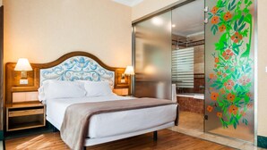 A hotel room with a bed, wooden headboard, two bedside lamps, a sliding glass door with a floral decal, and a wooden floor. - Hotel Julia (Madrid)