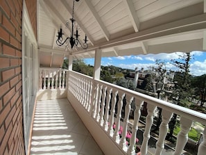 Un balcon couvert avec des balustrades blanches, un lustre noir suspendu et une vue sur un quartier résidentiel avec des maisons et des arbres.