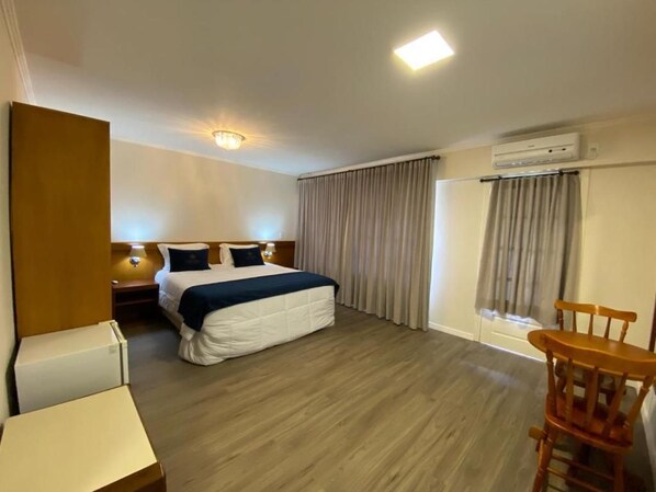 Una habitación de hotel con cama, mesita de noche, silla y ventana con cortinas.