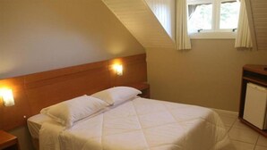 A single bed with a quilted white duvet in a room with a sloped ceiling and a small window with curtains. - Laponia Hotel Gramado (Gramado)