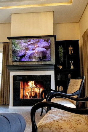 Een woonkamer met een open haard, een televisie erboven en een zwarte entertainmentkast met planken.