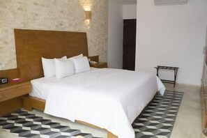 A bedroom with a wooden headboard, a large bed with white bedding, a nightstand, a bedside table, and a patterned rug. - Koox Casona de las 3 Marías Boutique Hotel (Mérida)