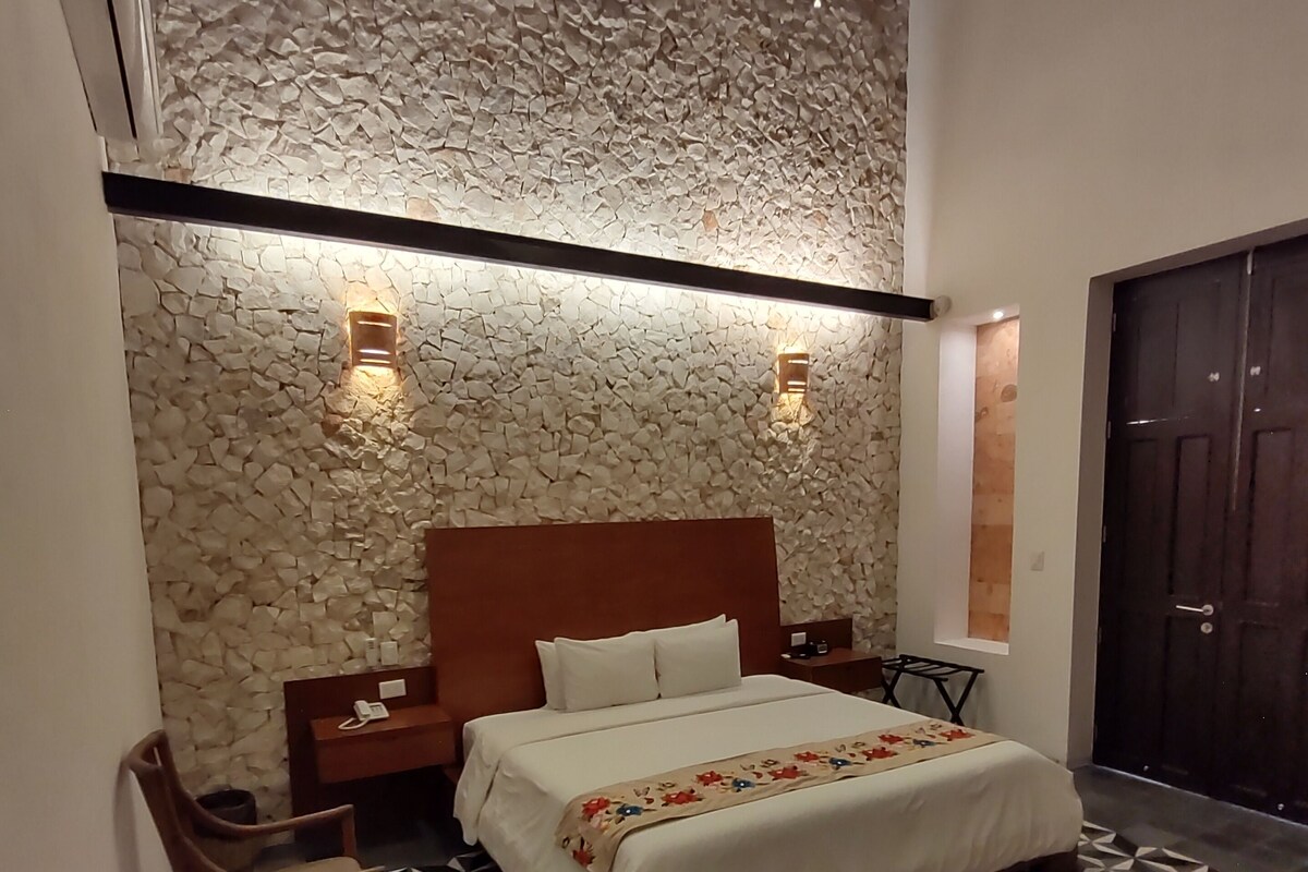 A bedroom with a stone wall, a bed, a nightstand, a chair, and a door.