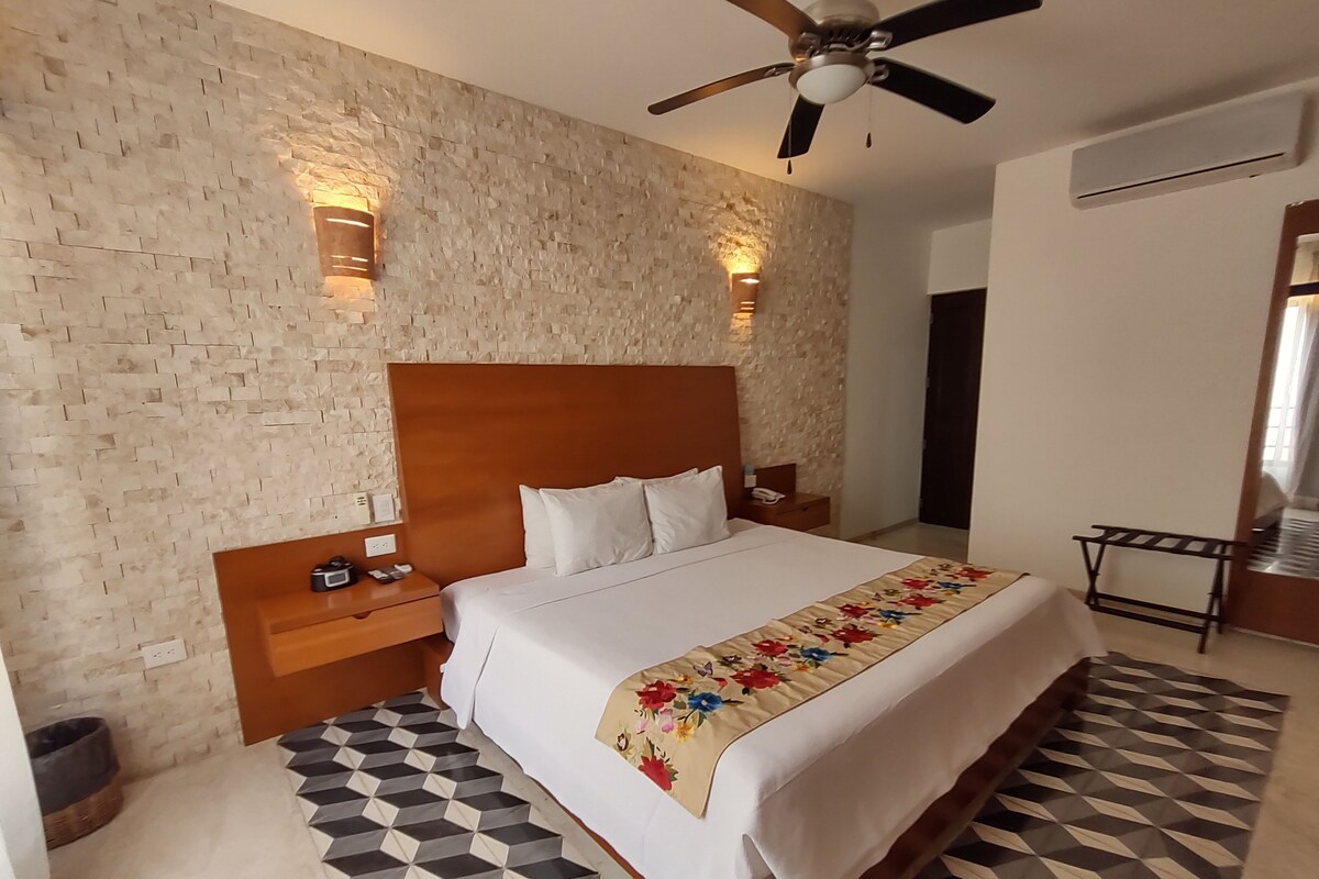 A hotel room with a brick-patterned wall, a wooden headboard, a bed with white bedding, a ceiling fan, and a patterned floor.