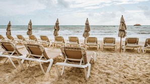 A beach with rows of white lounge chairs and beige umbrellas, facing the ocean. - Hotel Mimi Del Mar (Playa del Carmen)
