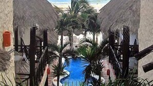 A pool area with a view of the beach, surrounded by palm trees and thatched-roof structures. - Hotel Mimi Del Mar (Playa del Carmen)