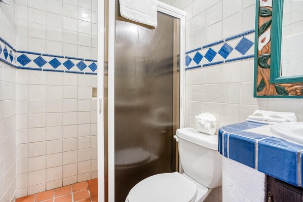 Bagno rivestito di piastrelle bianche, con doccia, wc e lavabo con piastrelle blu e bianche.