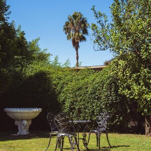 Ein Garten mit Tisch und Stühlen, einer großen Zierurne und einer Palme.