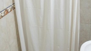 Une salle de bain avec un rideau de douche blanc, des toilettes blanches et un mur carrelé agrémenté d’une bordure décorative.