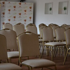 Des rangées de chaises beiges aux montures dorées sont disposées dans une salle de conférence.