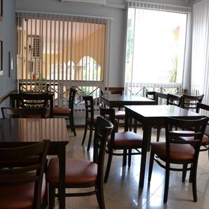 A restaurant interior with multiple tables and chairs, large windows with blinds, and a view of the outside. - Solares Del Alto Hotel And Spa (Alta Gracia)