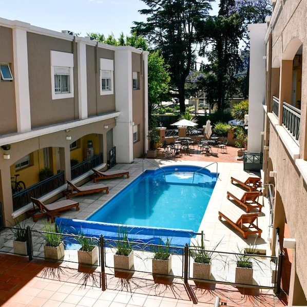 A swimming pool with lounge chairs, a covered seating area, and potted plants.