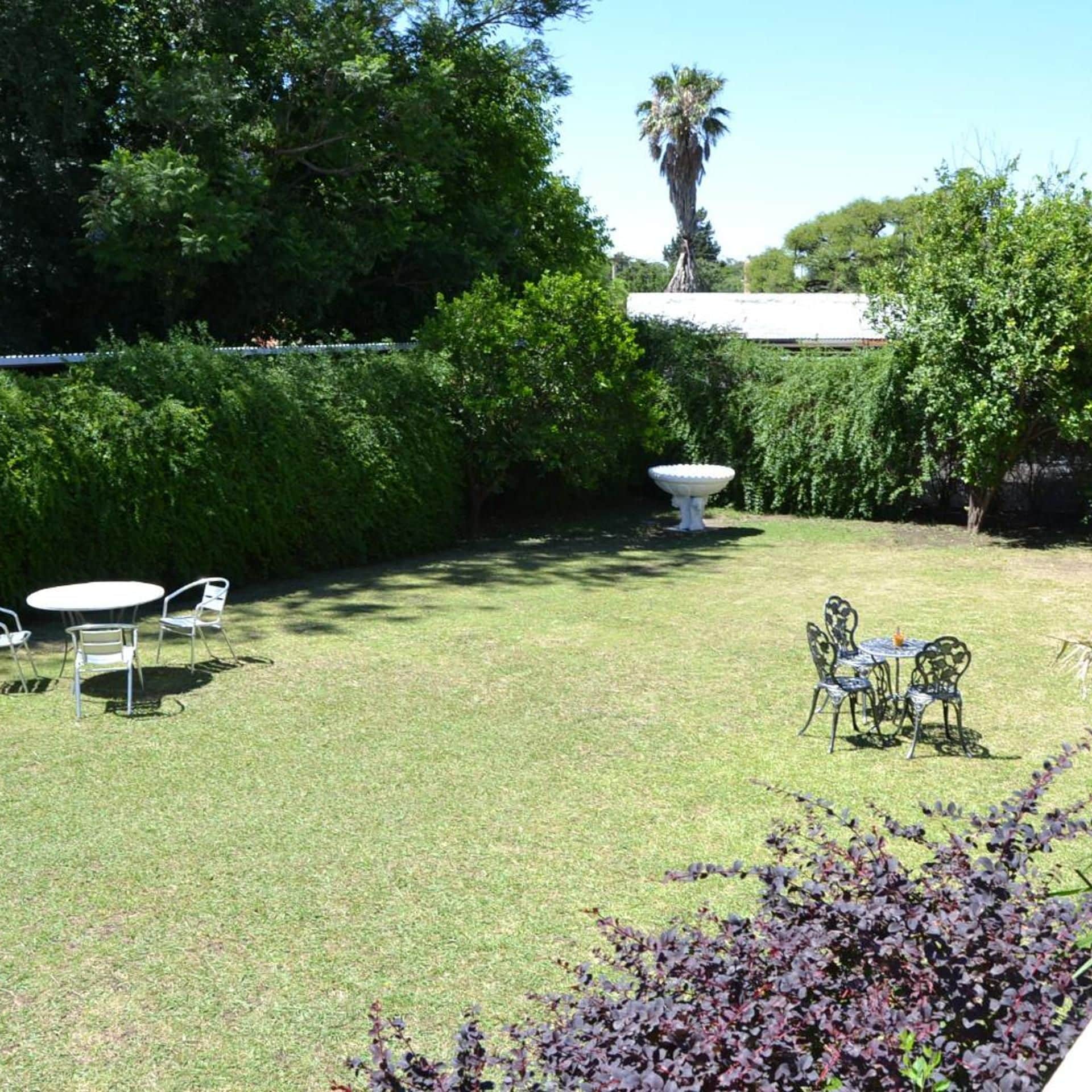 Un jardín bien cuidado con césped, dos mesas con sillas y una maceta decorativa grande.