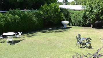 Un jardín bien cuidado con césped, dos mesas con sillas y una maceta decorativa grande.
